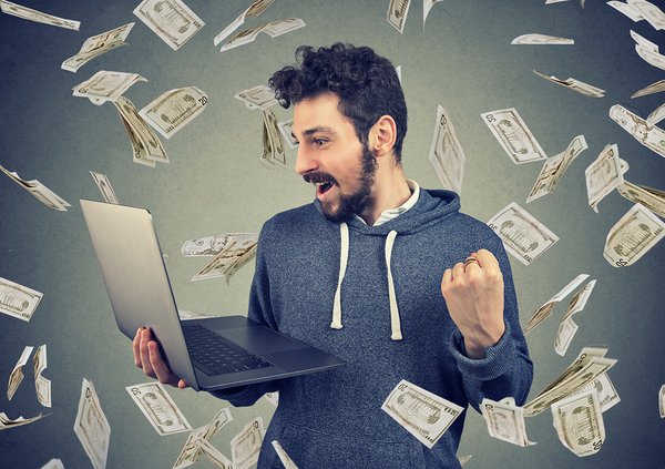 Man holding a laptop with paper money falling down around him.